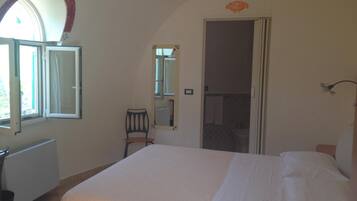 A bedroom with a bed, a chair, a radiator, a window, and a mirror.