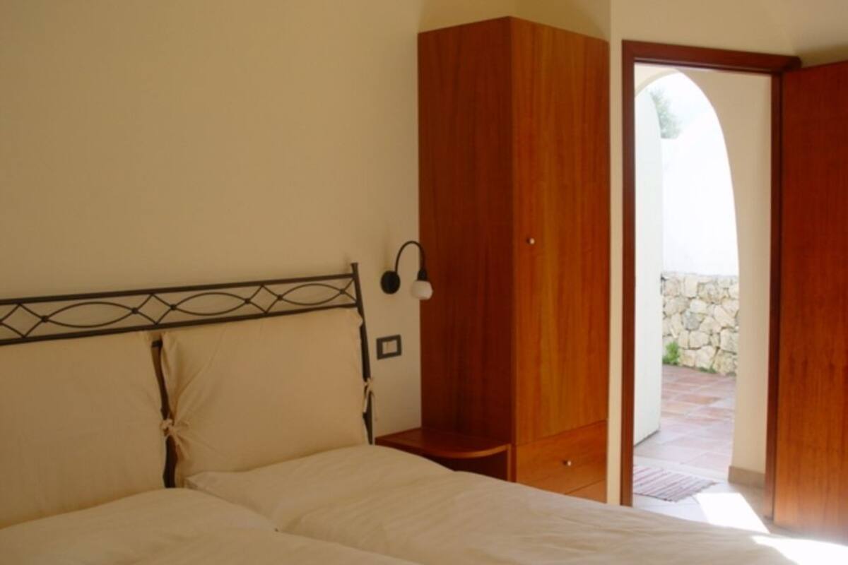 Une chambre à coucher comprenant un lit, une armoire en bois, une table de chevet et une porte donnant sur un espace extérieur.