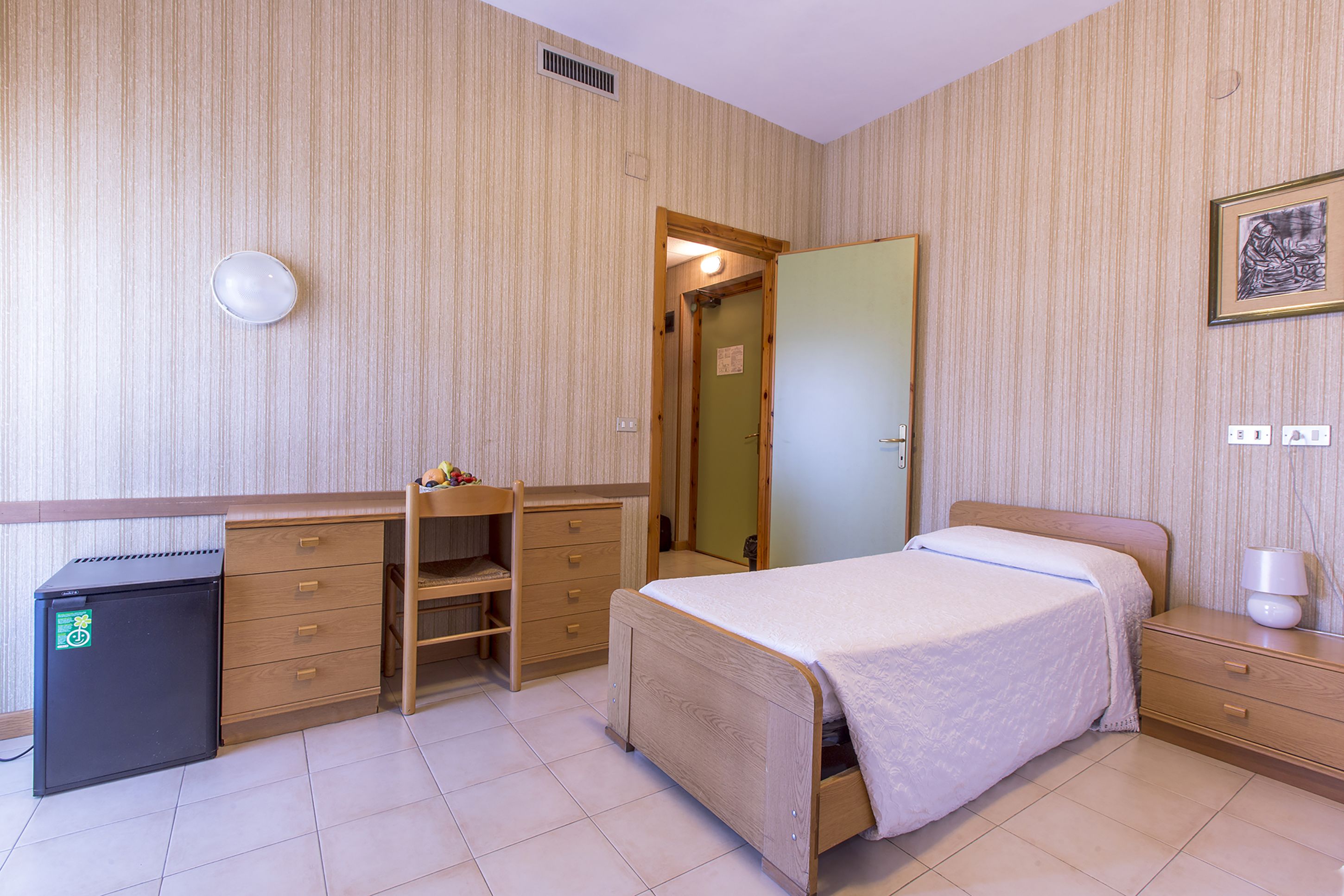 A bedroom with a bed, a desk, a dresser, and a small refrigerator.