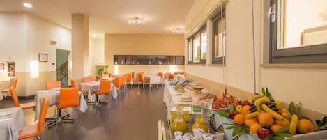 Un comedor con mesas y sillas, un bufé con frutas y bebidas, y una ventana con vistas.