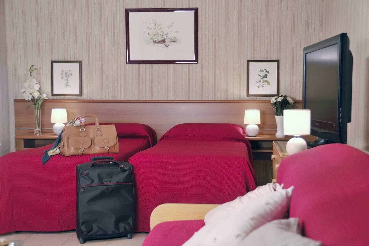 A hotel room with two beds, a TV, and a desk with a lamp and a vase of flowers.