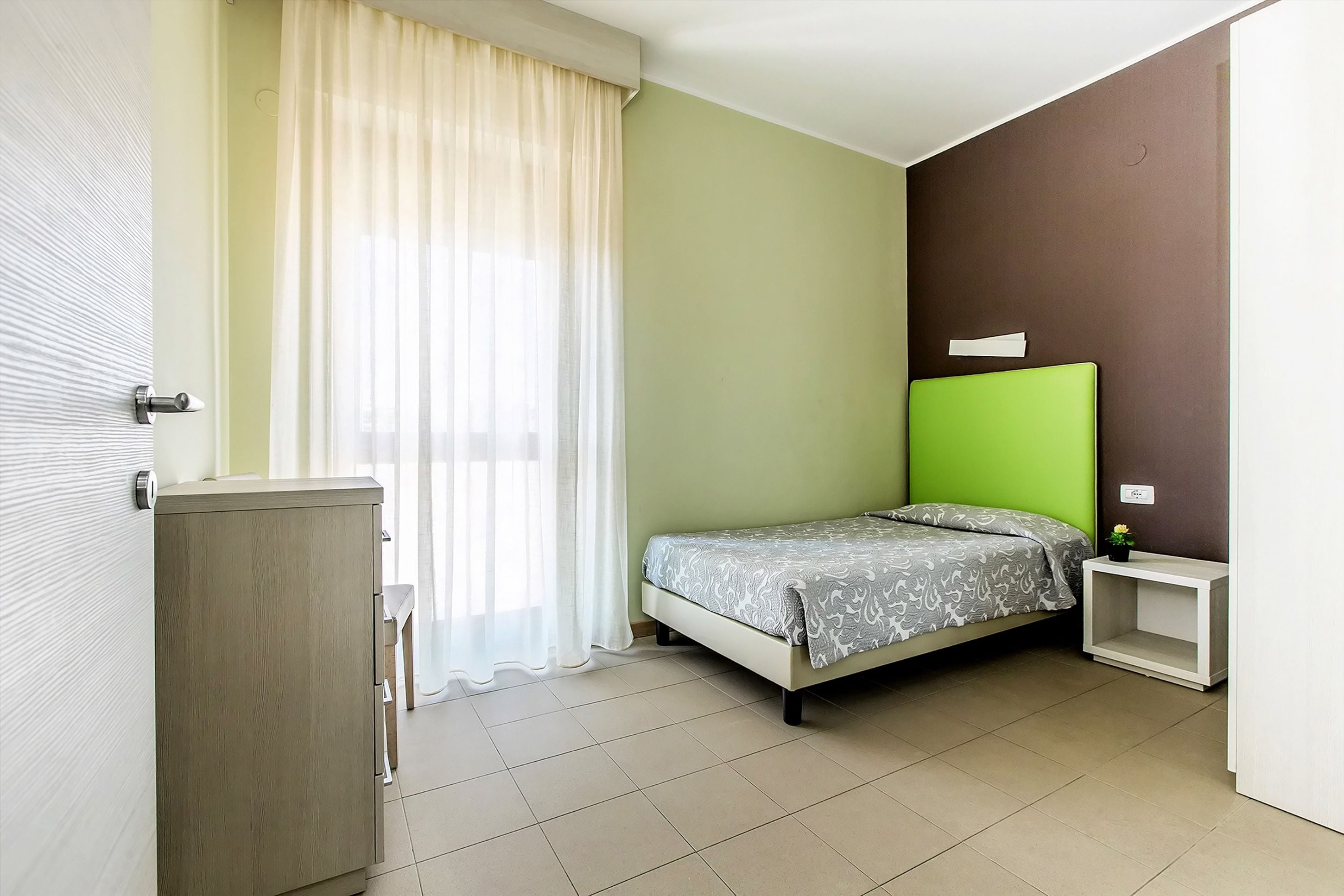 A bedroom with a bed, a nightstand, a cabinet, and a window with curtains.