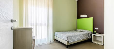 A bedroom with a bed, a nightstand, a cabinet, and a window with curtains.