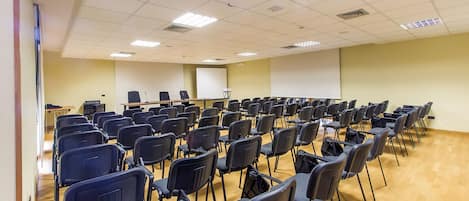 Un salón de conferencias con filas de sillas, una pantalla de proyector y un atril.