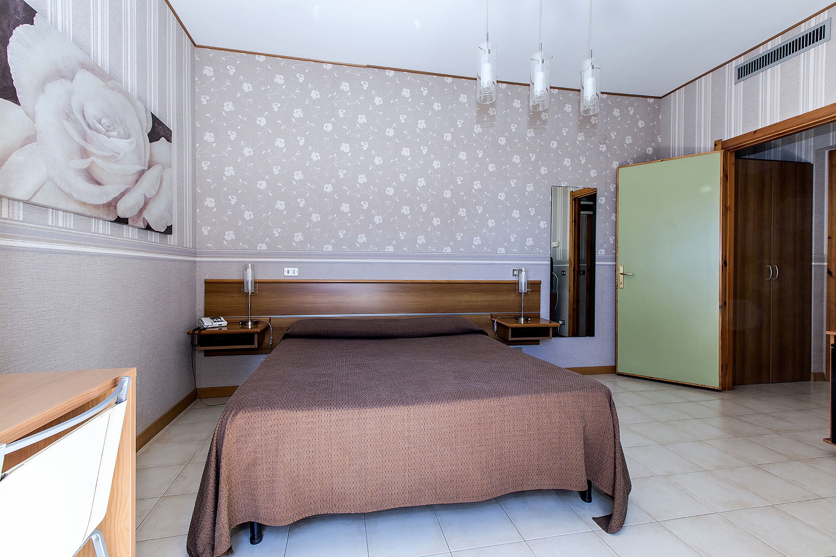 A bedroom with a large bed, bedside tables, a nightstand, a mirror, and a wardrobe.