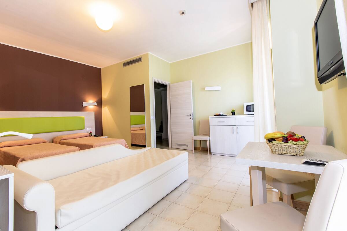 A hotel room with a bed, a desk, a chair, a television, and a small kitchenette.