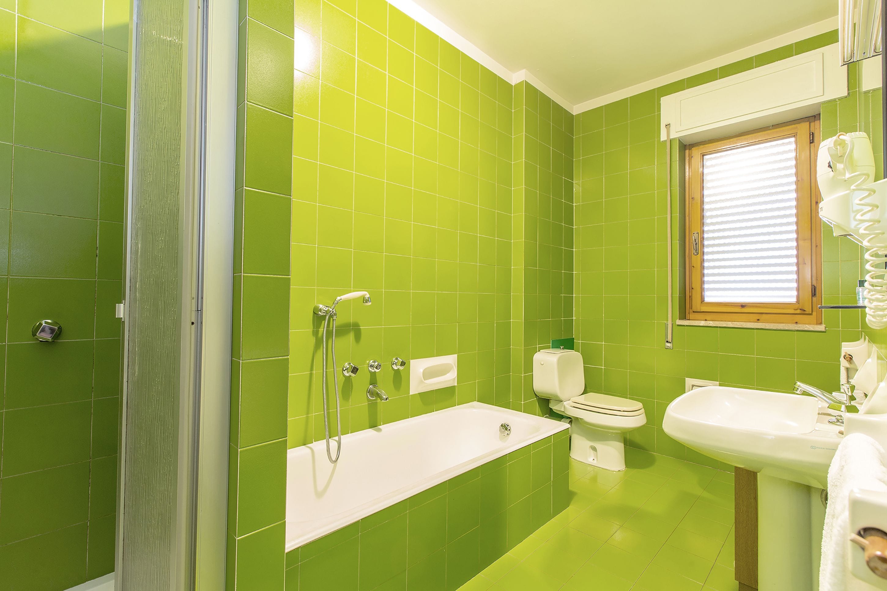 A bathroom with green tiles, a bathtub, a toilet, and a sink.