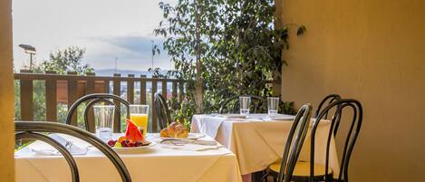 Un área de comedor al aire libre con mesas dispuestas para el desayuno, mostrando croissants y zumo de naranja.