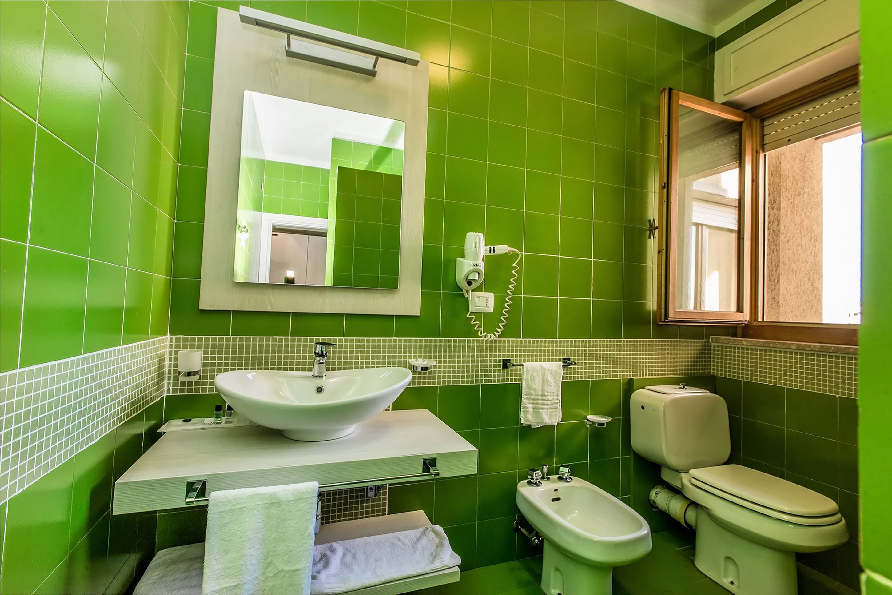 A bathroom with green tiles, a white sink, a bidet, and a toilet.