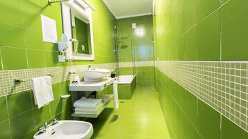 Een smalle badkamer met groene tegels, een witte wastafel, een spiegel en een douchehoek.