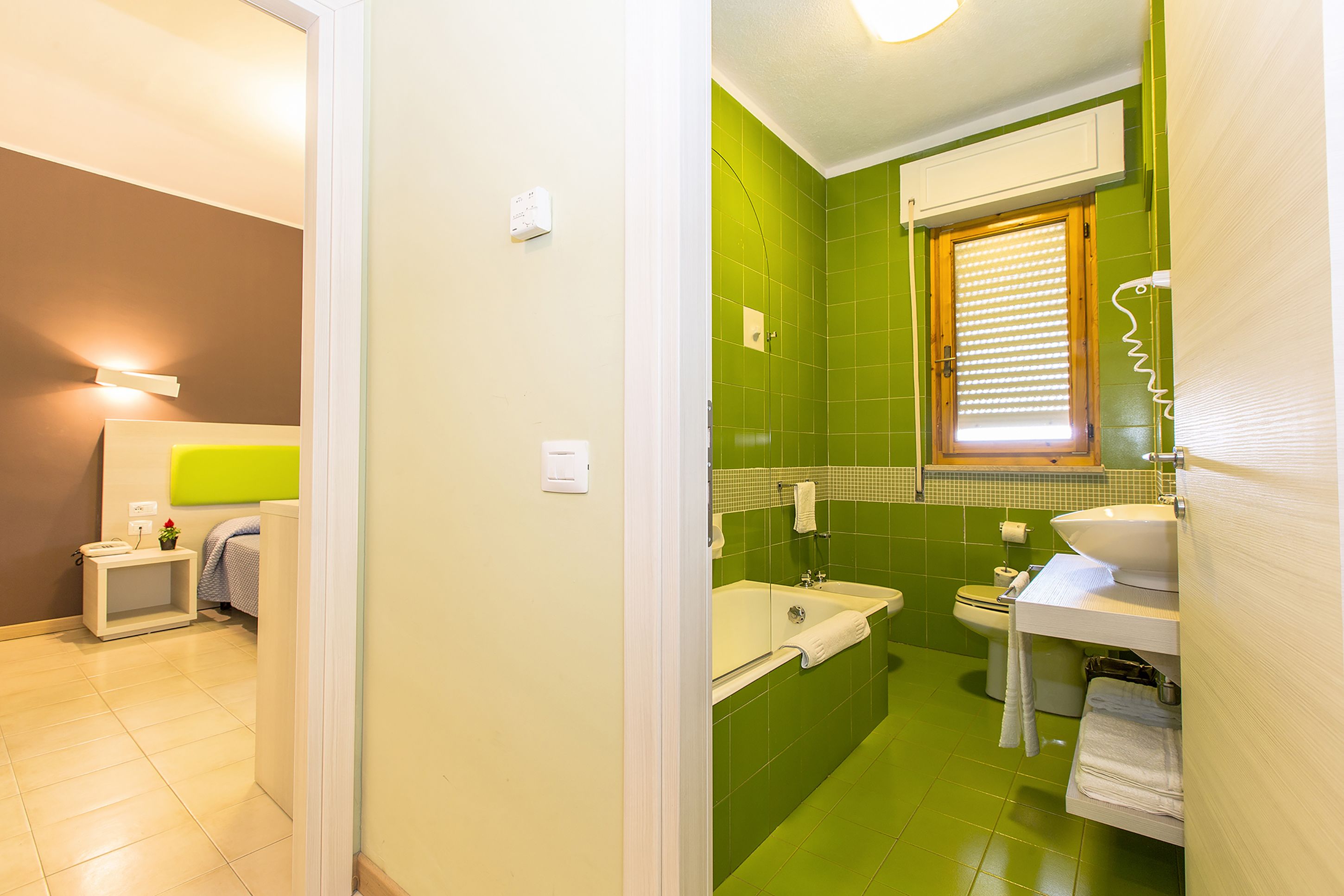 Une salle de bain avec un mur recouvert de carreaux verts, un lavabo blanc, des toilettes blanches et une baignoire.