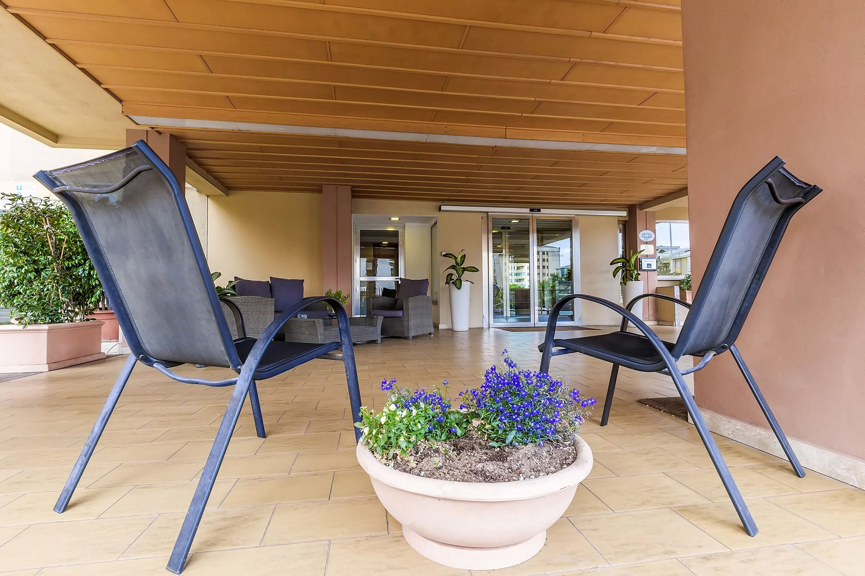 A covered outdoor seating area with two chairs and a large planter with flowers.