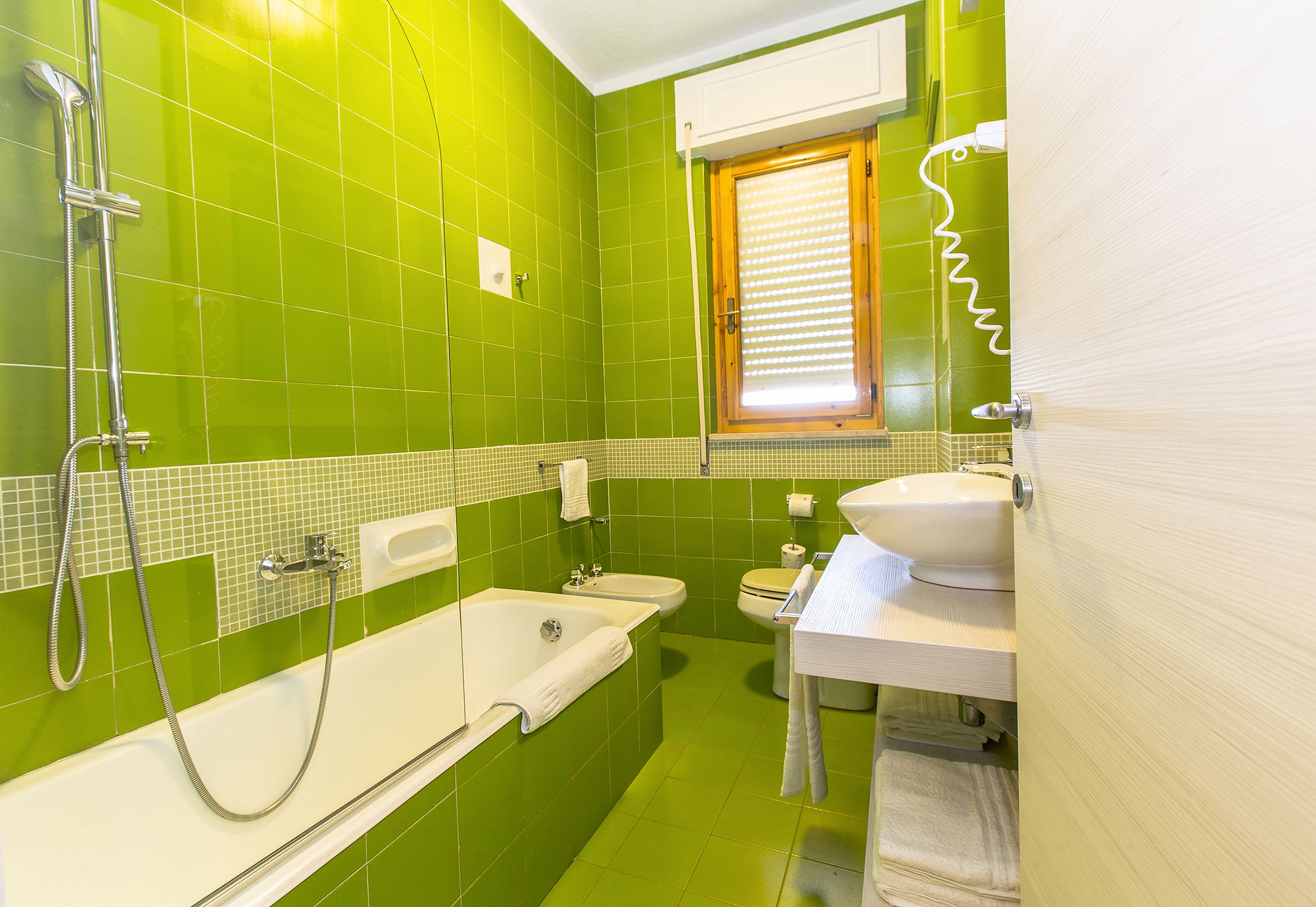 A bathroom with green tiles, a bathtub, a sink, and a toilet.