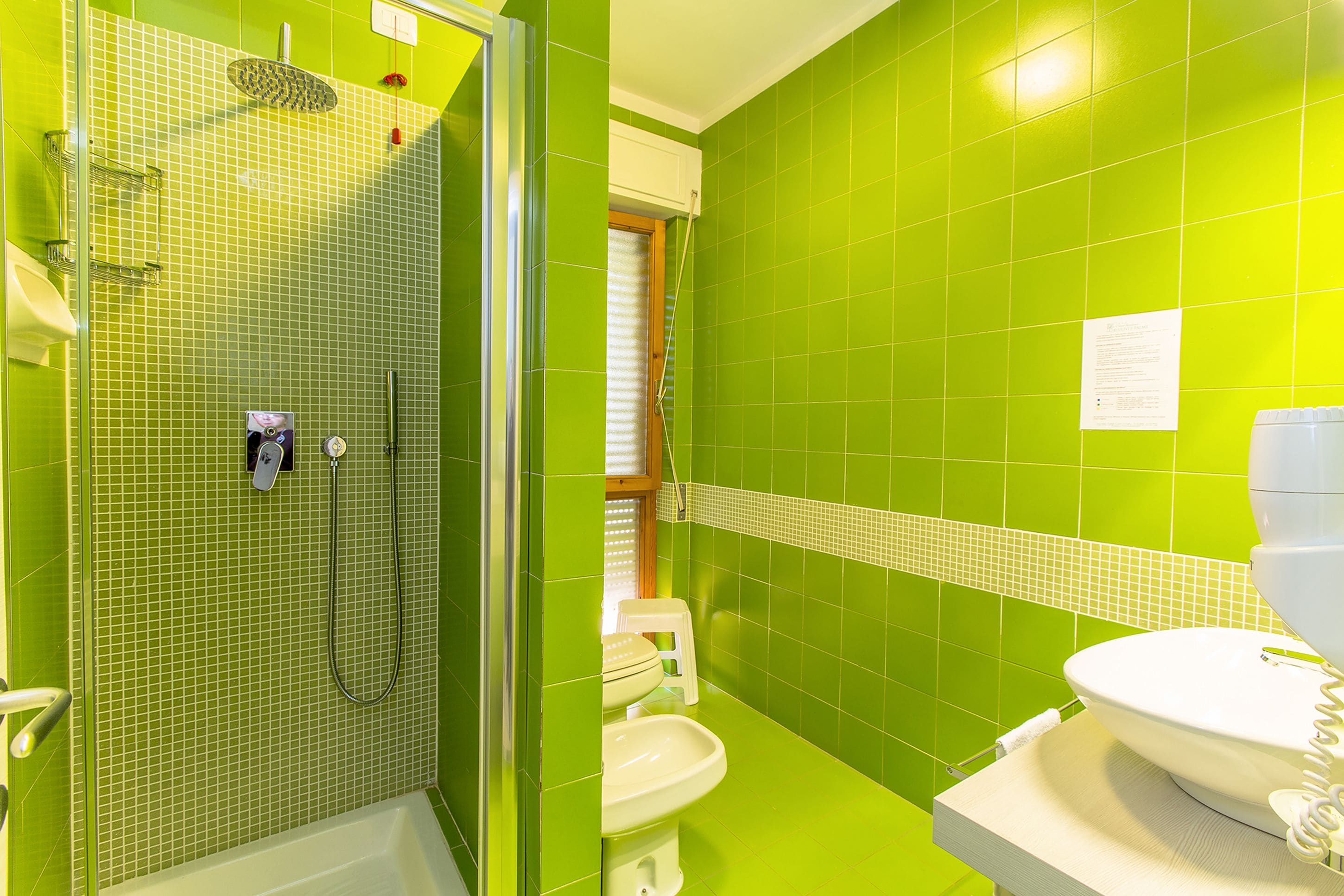 Ein Badezimmer mit grünen Fliesen, einer Dusche, einer Toilette und einem Waschbecken.