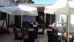 An outdoor patio area with black chairs and tables, white umbrellas, and potted plants. - Borgo Pida (Misiliscemi)