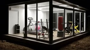 A modern gym with exercise equipment, including a treadmill, weights, and a punching bag, enclosed in a glass-walled structure. - Borgo Pida (Misiliscemi)