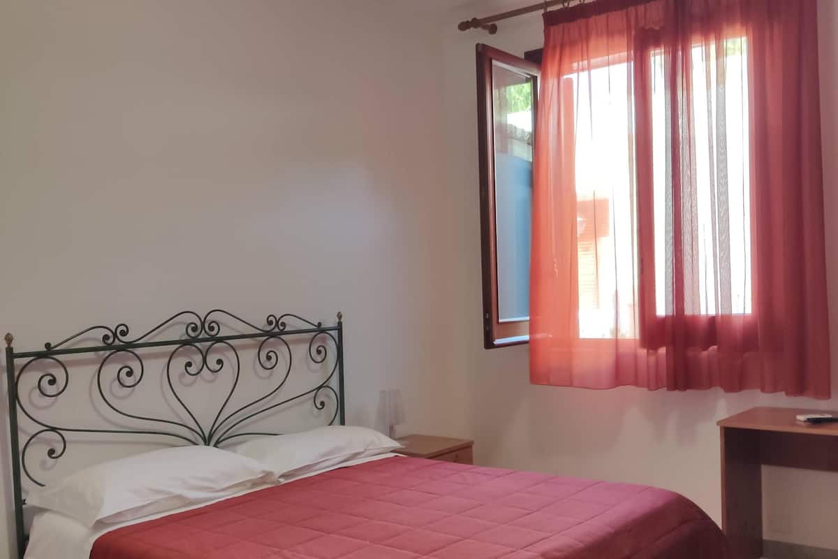 Una camera da letto con un letto, un comodino, una scrivania e una finestra con tende.