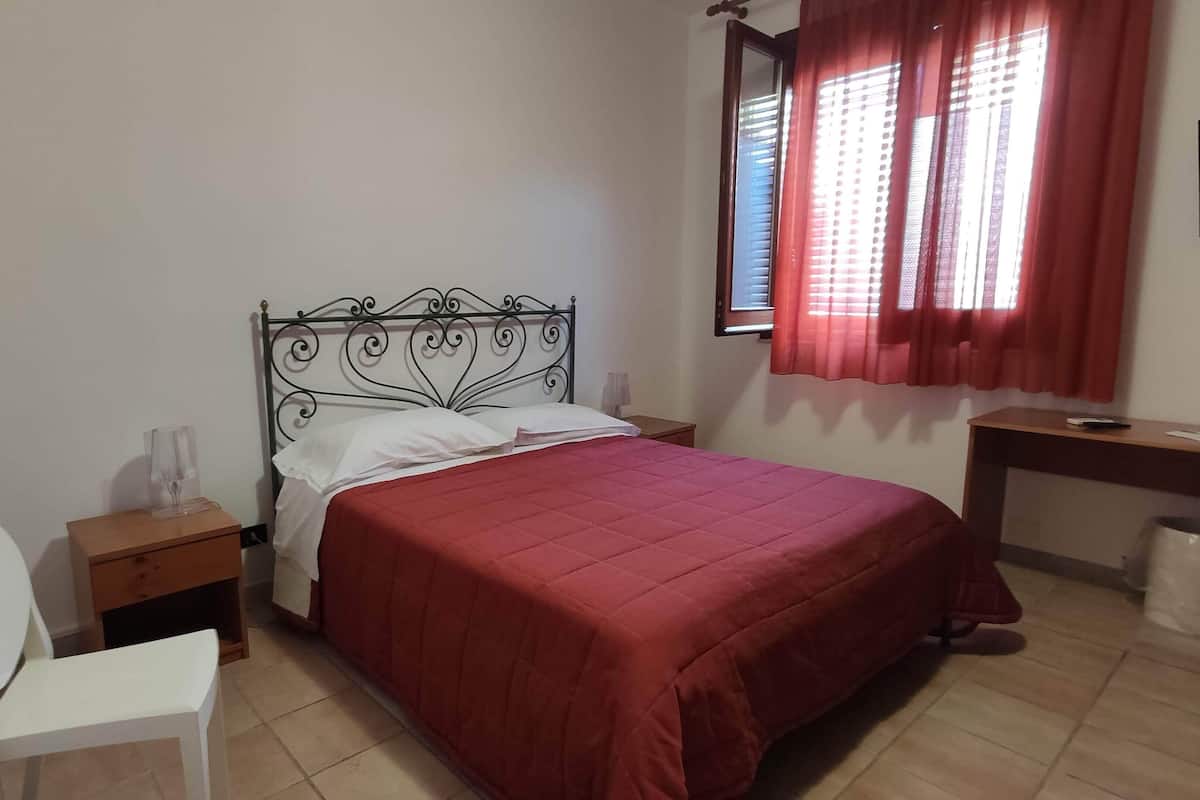 Una camera da letto con un letto, una scrivania, una sedia, un comodino e una finestra con tende.