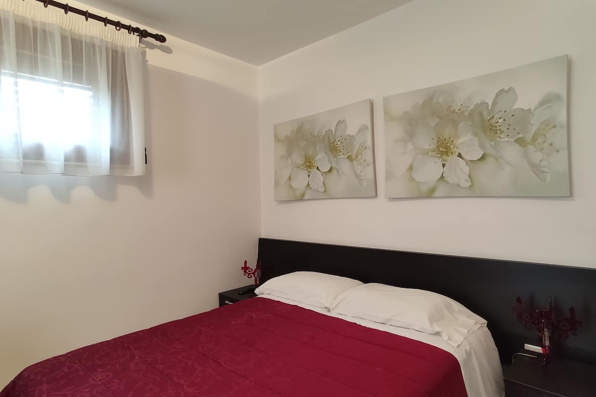 Una camera da letto con una copriletto rosso, cuscini bianchi e due quadri con fiori appesi al muro.