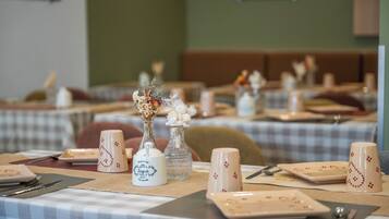 A dining area with tables set for service, featuring checkered tablecloths and white plates with red patterns.