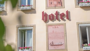 Fachada de hotel con múltiples ventanas, algunas con jardineras, y un letrero llamativo que dice 'hotel'.