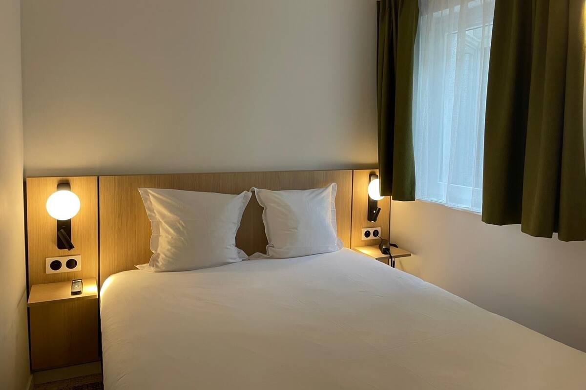 A hotel room with a bed, two bedside tables, and two wall-mounted lamps.