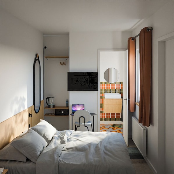 Un dormitorio con cama, escritorio con computadora, silla, espejo y baño visible a través de una puerta abierta.