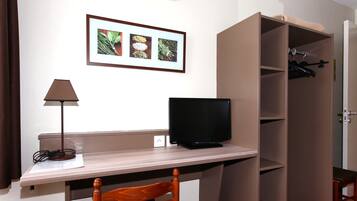 A room with a desk, a television, a chair, a wardrobe, and a framed picture on the wall.