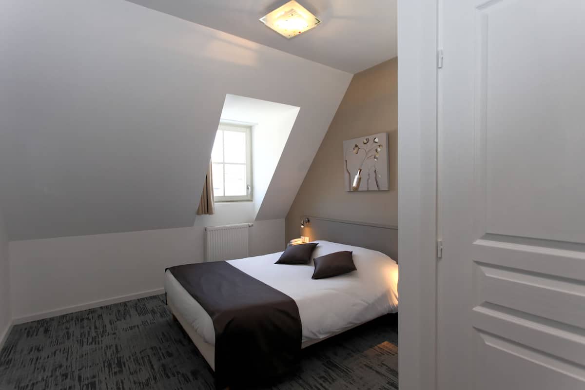 A bedroom with a bed, a window, and a wall-mounted artwork.
