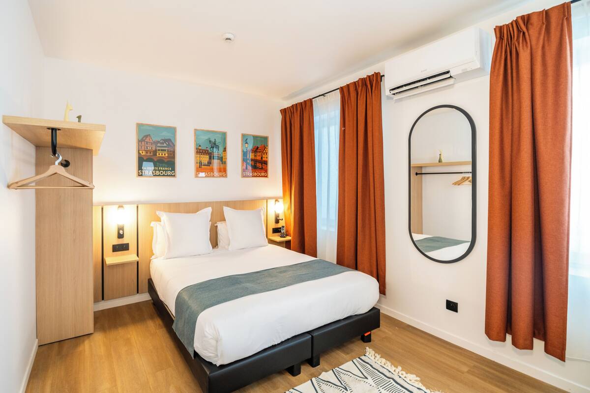 A hotel room with a bed, a wardrobe, a mirror, and wall-mounted artwork.