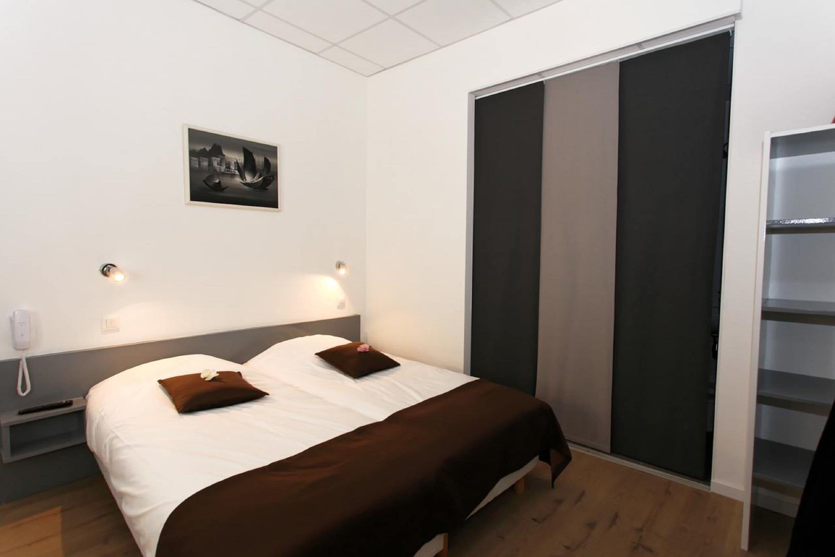A hotel room with a bed, bedside lamps, a nightstand, a phone, a picture on the wall, and a sliding door closet.