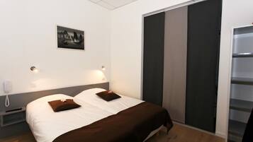 A hotel room with a bed, bedside lamps, a nightstand, a phone, a picture on the wall, and a sliding door closet.