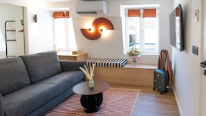Una sala de estar moderna con un sofá gris, una mesa de centro redonda negra, un televisor montado en la pared y una ventana con cortinas.