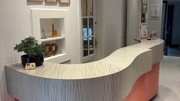 A reception desk with a curved design, a potted plant, and framed certificates on the wall.