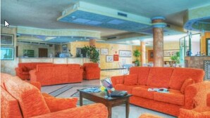 A lobby with orange sofas, a reception desk, and a coffee table. - Hotel Baia Marina (Orosei)
