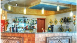 A bar area with a tiled backsplash, hanging pendant lights, and a variety of bottles and glasses on shelves. - Hotel Baia Marina (Orosei)