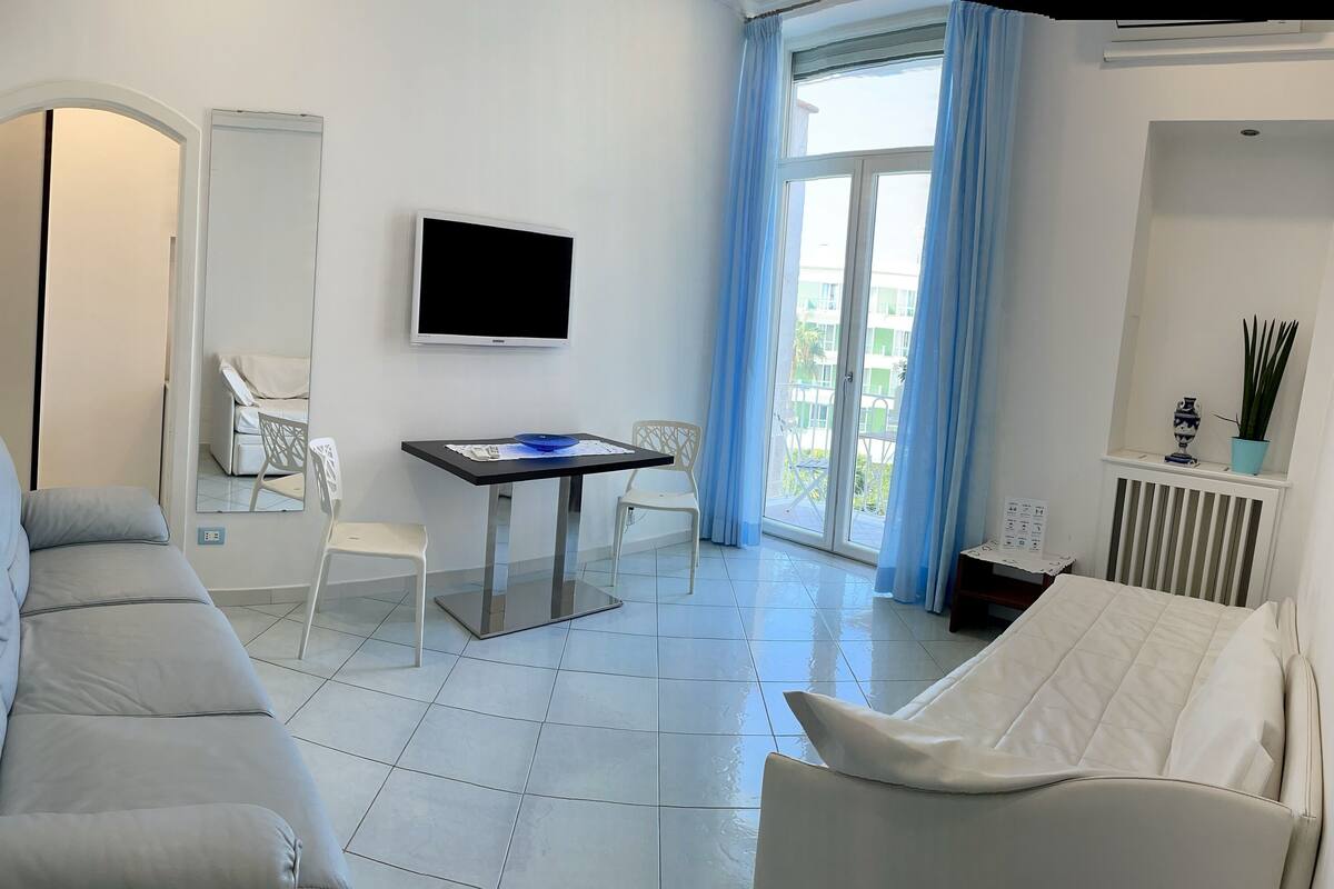 Una camera d'hotel moderna con un divano grigio, una poltrona bianca, un tavolino e una TV a parete.