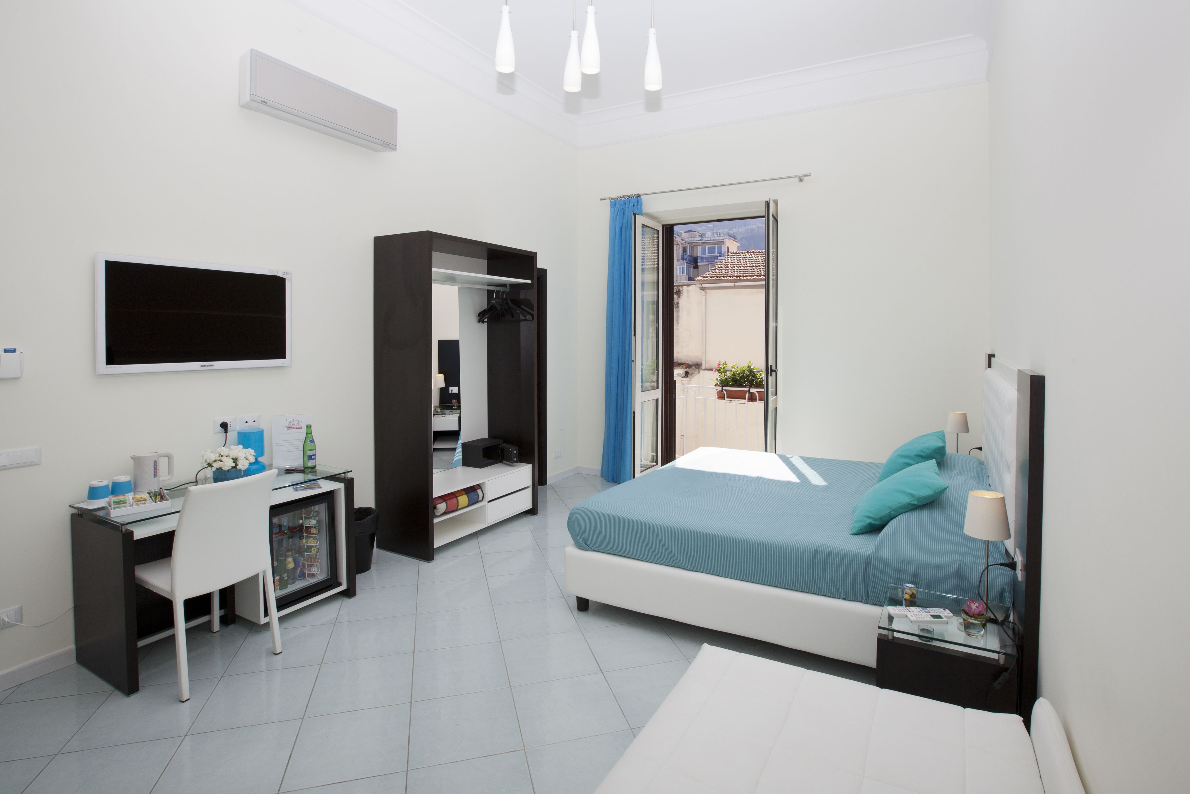 Quarto moderno com cama, escrivaninha, guarda-roupa e televisão.