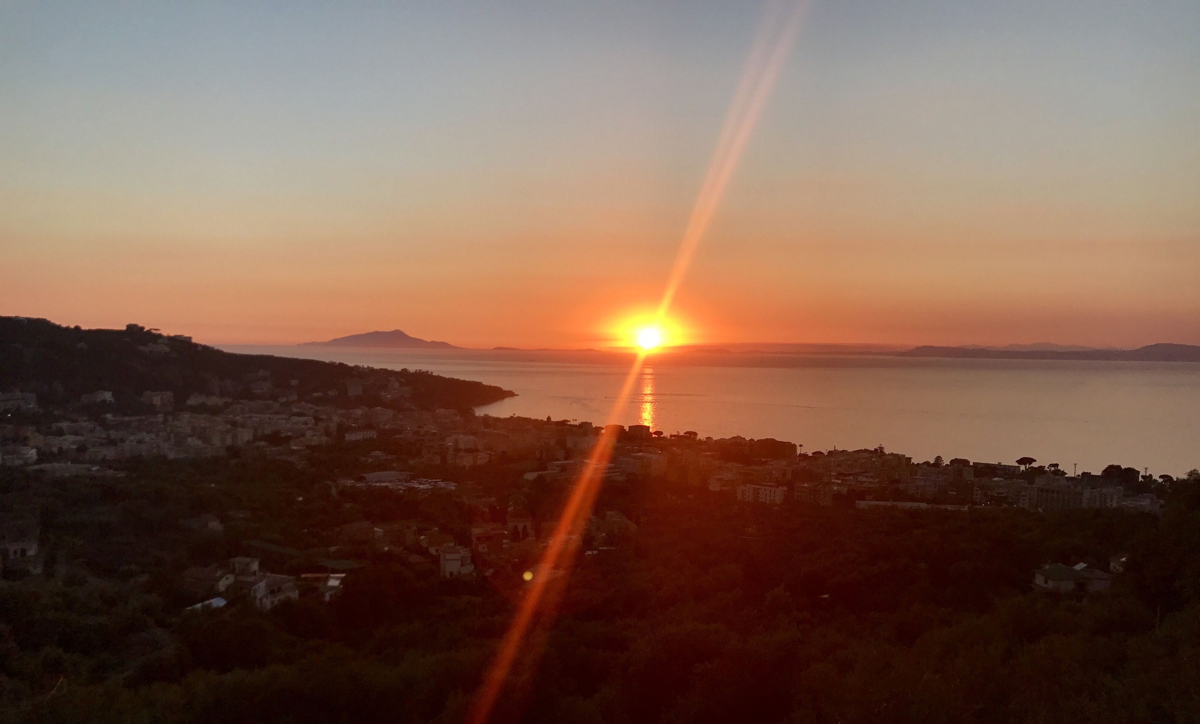 A sunset over a coastal city with buildings and hills in the foreground.