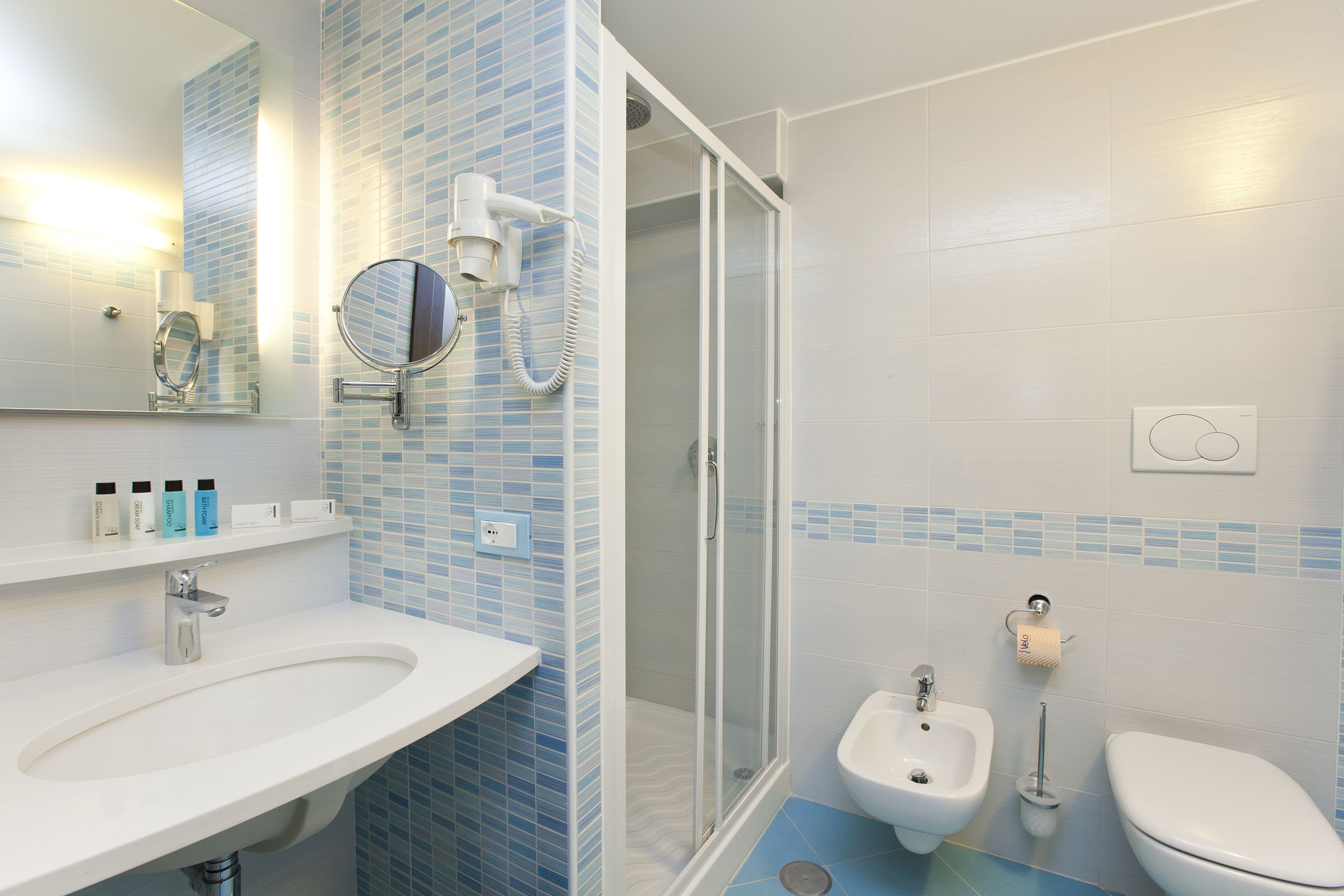 A bathroom with a sink, mirror, hairdryer, bidet, toilet, and a shower area.