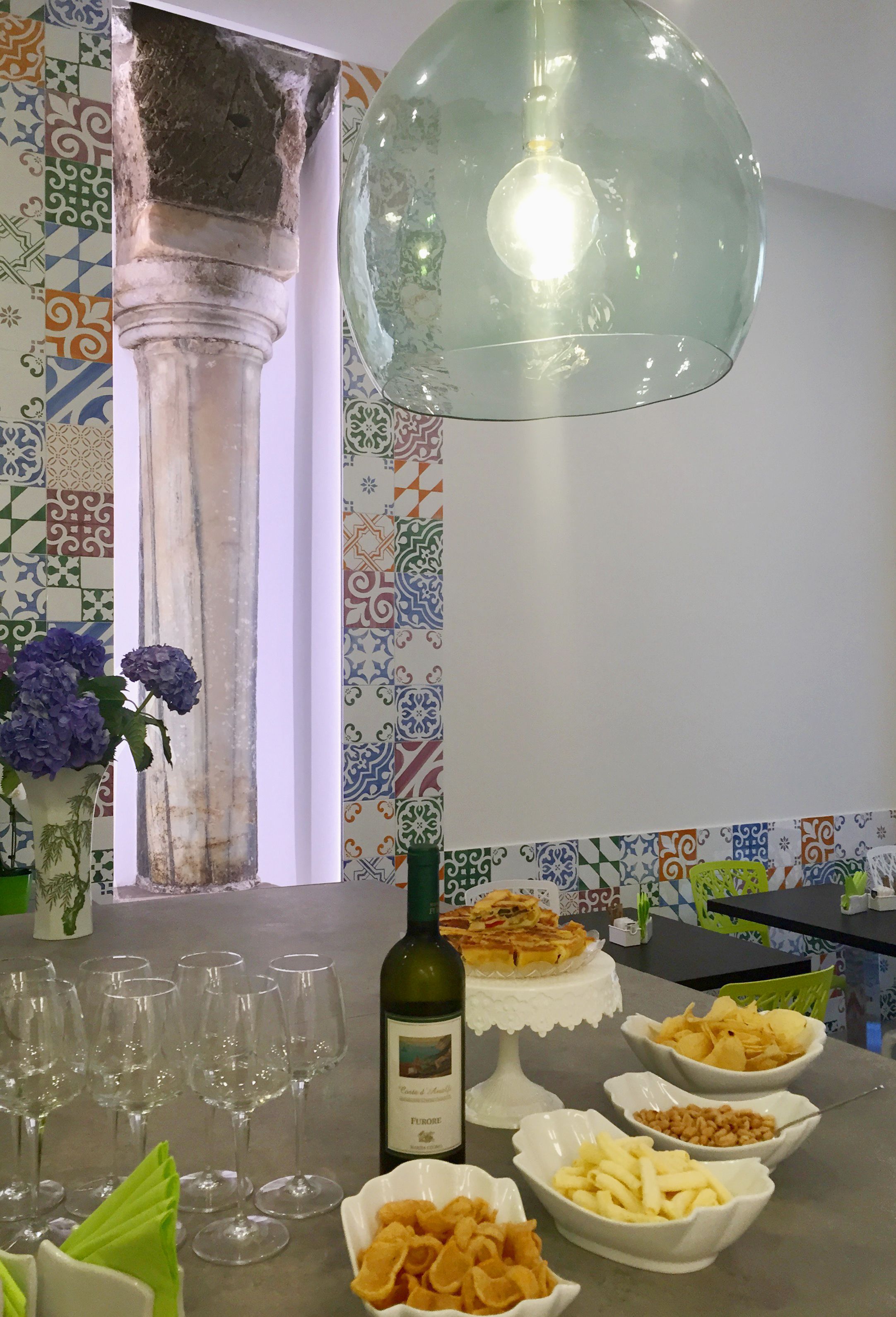 A dining table with wine glasses, a bottle of wine, and various snacks.