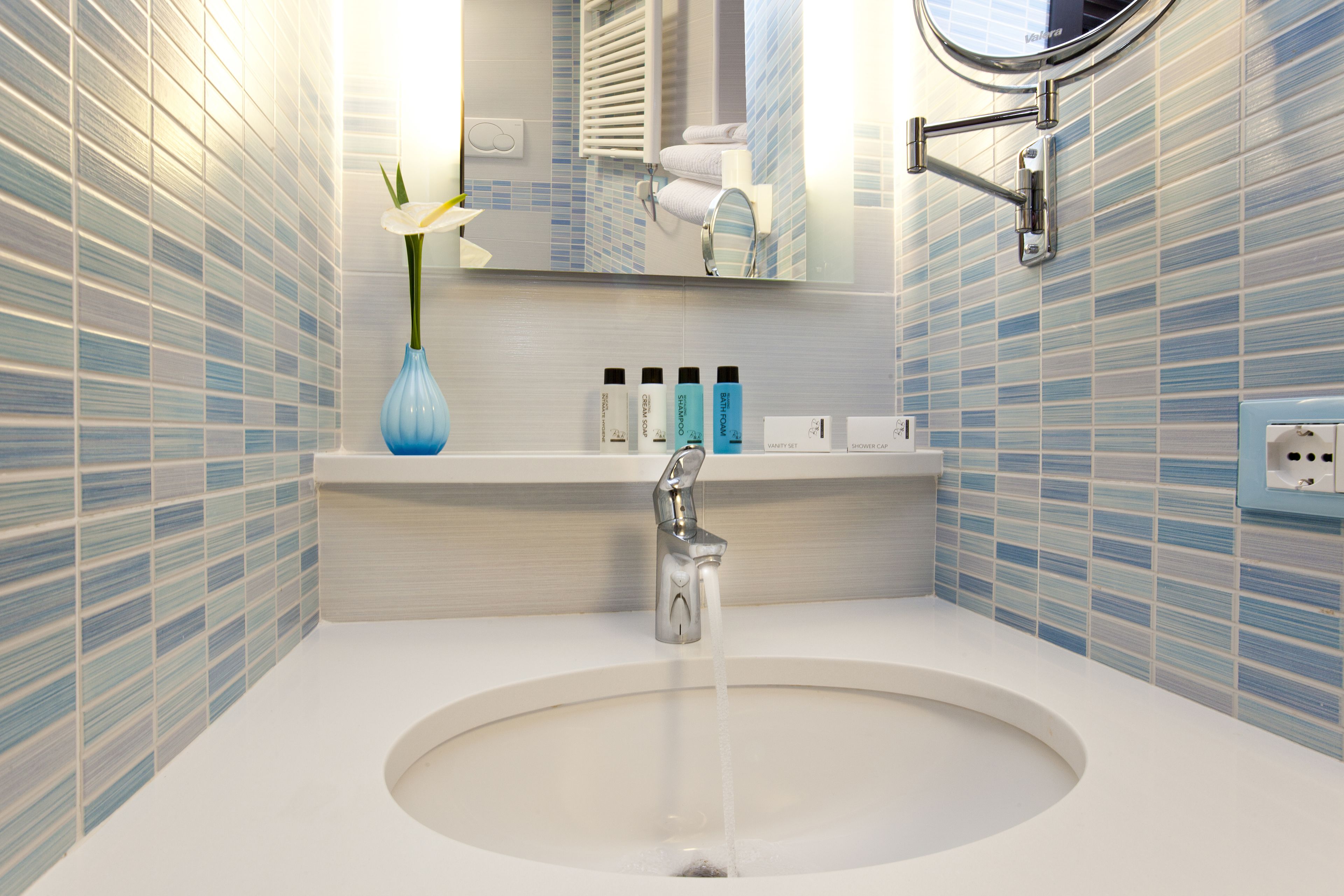 A bathroom with a round sink, a mirror, and a blue vase with a white flower.