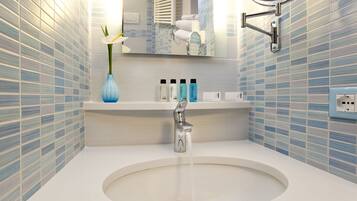 A bathroom with a round sink, a mirror, and a blue vase with a white flower.