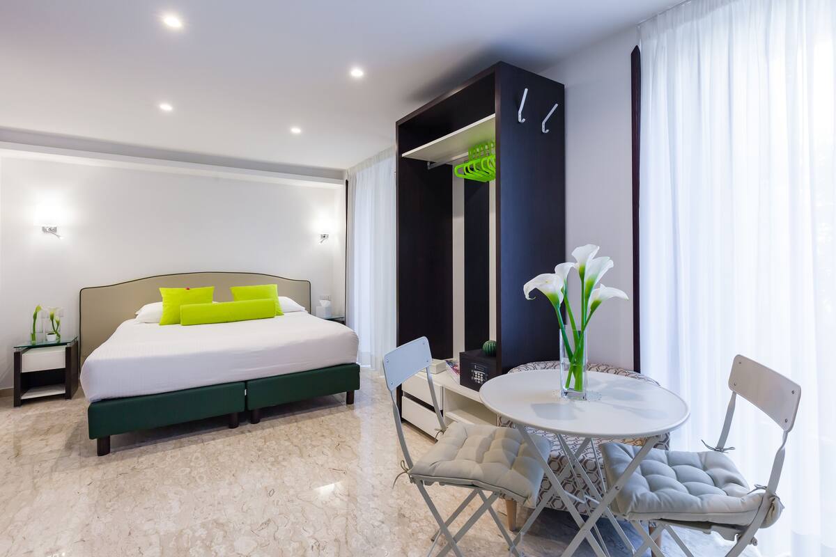 Una moderna camera d'albergo con un letto, un'area pranzo con sedie, un tavolino e un vaso con fiori.