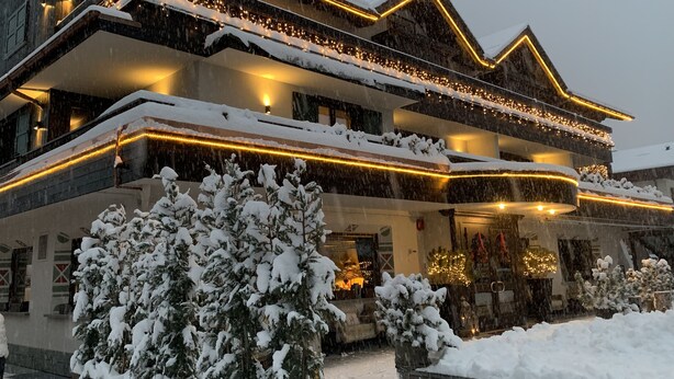 A multi-story hotel with a snow-covered exterior, illuminated by warm lights, and surrounded by snow-laden trees. - Hotel Alù (Bormio)