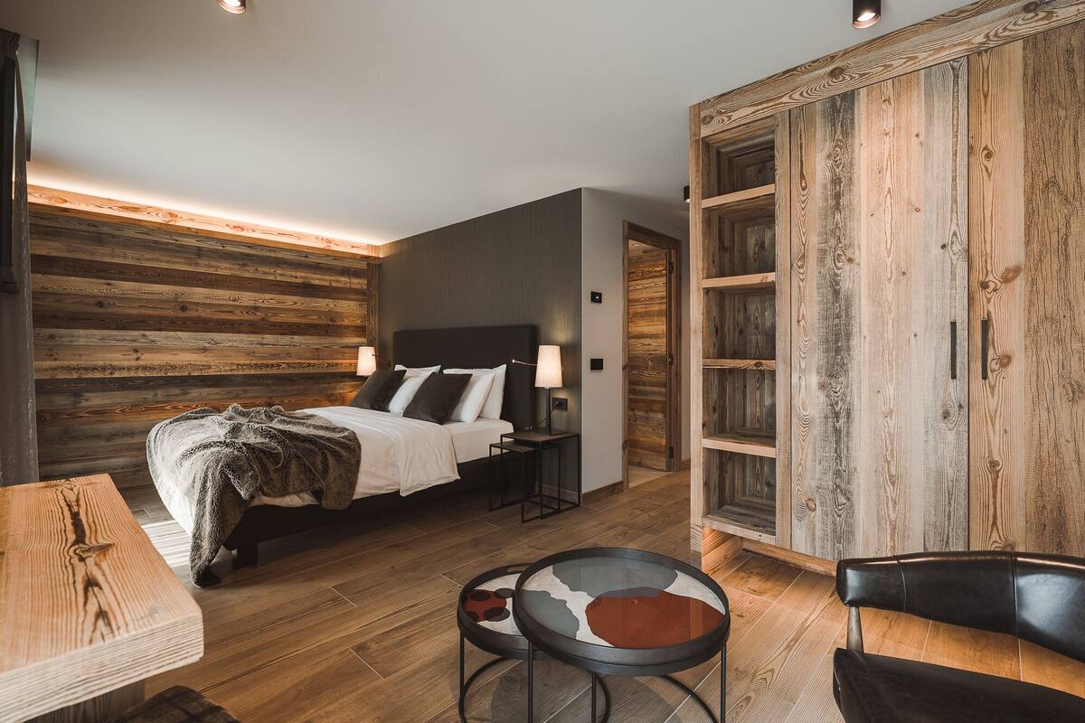Un dormitorio moderno con una pared de madera, una cama con ropa blanca, una mesita de noche, una lámpara y un armario de madera.