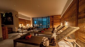A modern spa room with wooden walls, a large window overlooking a pool, and multiple loungers with towels. - Hotel Alù (Bormio)