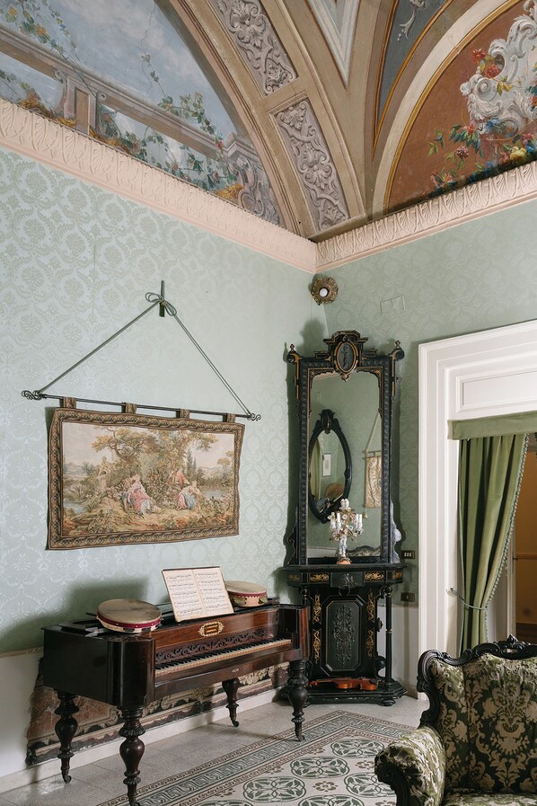 Ein Zimmer im klassischen Stil mit einem großen Spiegel, einem Klavier und einem gerahmten Gemälde an der Wand.