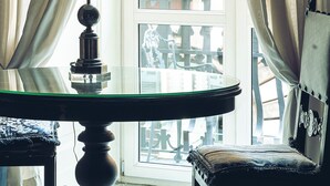 Una habitación con una mesa de vidrio, una lámpara y vistas a un edificio a través de una ventana con cortinas.