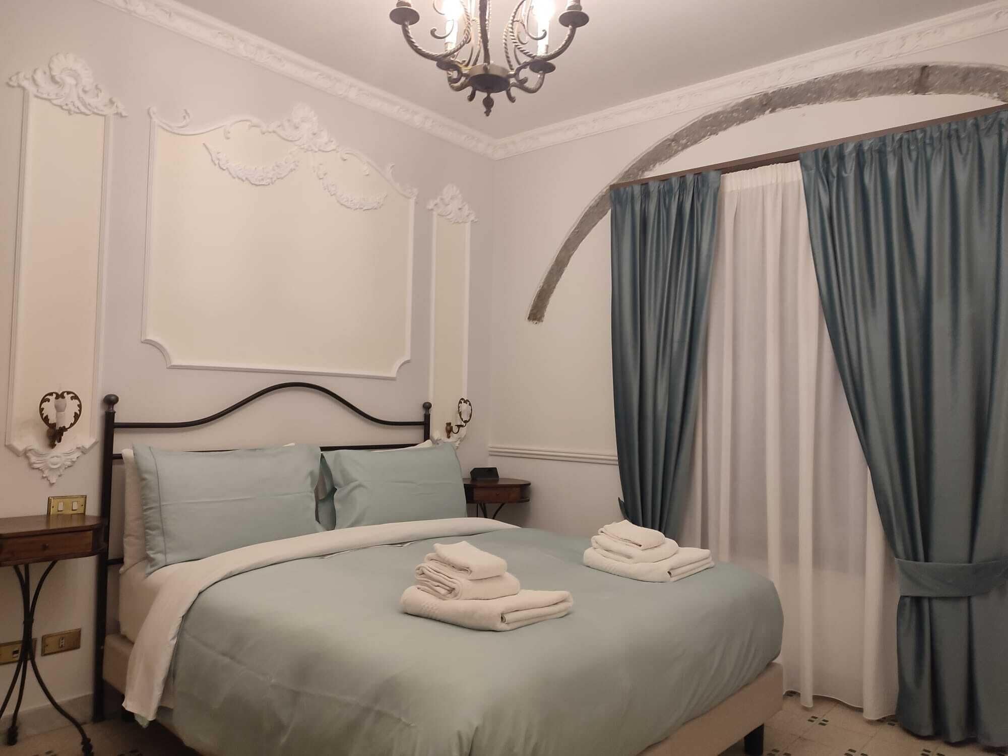 Una camera da letto con un letto, un comodino, un lampadario e tende.